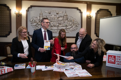 Piotr Grzymowicz, Prezydent Olsztyna z grupą wsp&oacute;łpracownik&oacute;w omawia kampanię informacyjną. Na stole widoczne materiały promocyjne. 